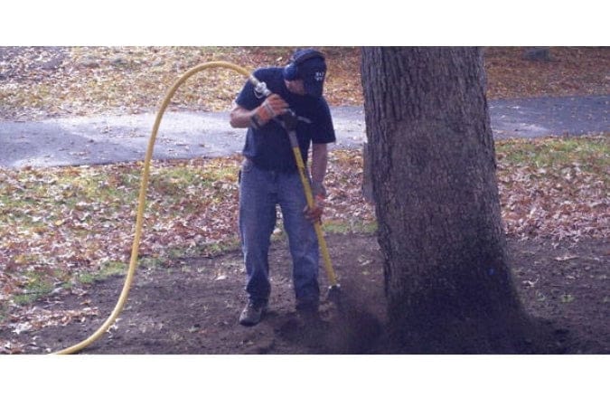 Person using an AirSpade by a tree in an outdoor setting