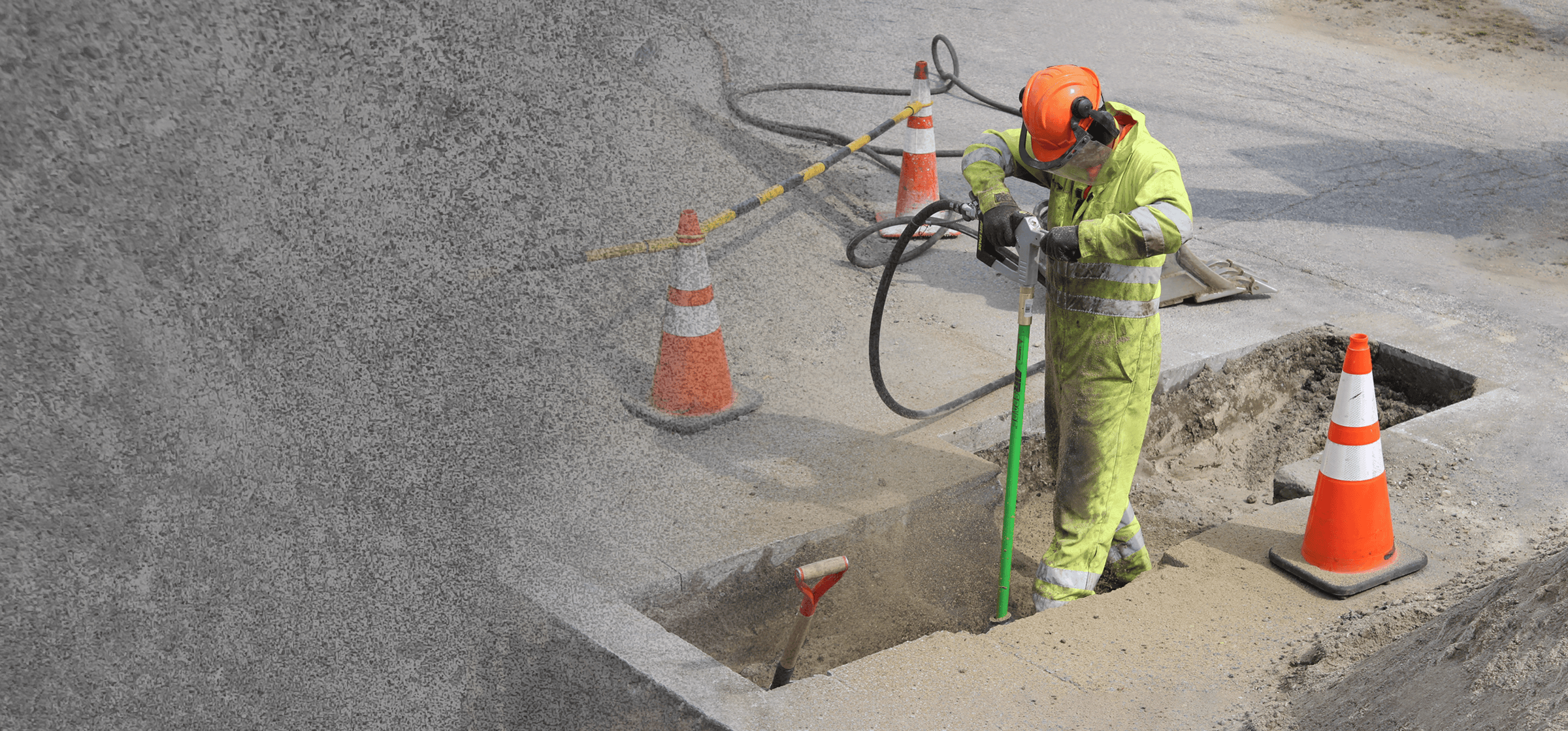 Person in high-visibility clothing working on a road with safety cones and tools.