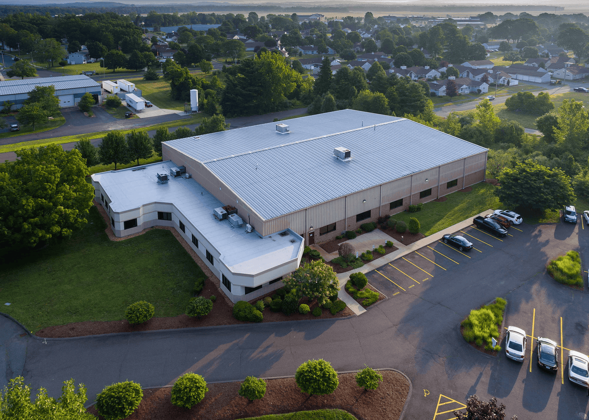 Aerial view of a large building with a parking lot and surrounding greenery.